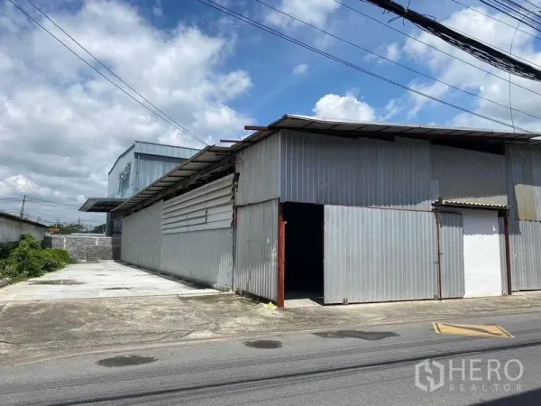 Warehouse for rent in Saphan Sung, Bangkok - Corrugated metal warehouse exterior with large sliding door and wide concrete driveway for loading and parking.