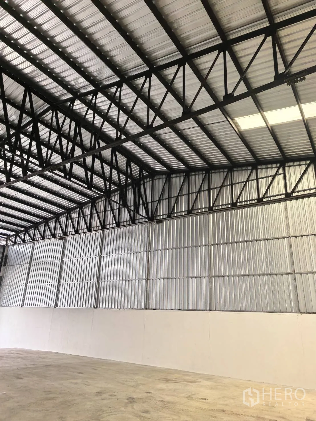 Warehouse for rent in Suan Luang, Bangkok - Close-up of steel truss roof and metal wall panels with a translucent roof panel for light.