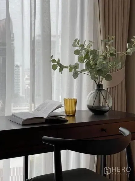 Condominium for rent or sale in Khlong Toei, Bangkok - Work desk by a tall window with an open book and glass vase, sheer drapes and skyline beyond.