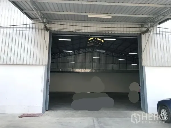 Warehouse for rent in Pak Kret, Nonthaburi - Wide entry with metal canopy and tall sliding doors opening to a well-lit warehouse space and loading area.