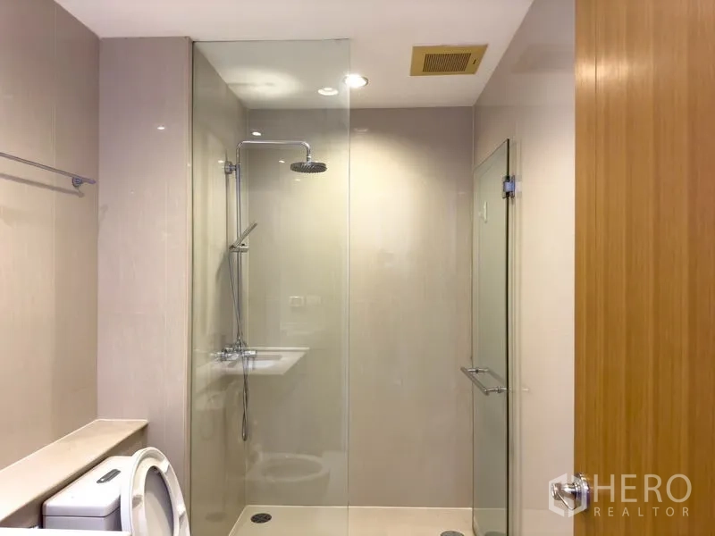 Condominium for rent or sale in Pathum Wan, Bangkok - Glass‑enclosed shower with rain head and minimalist beige tiles.