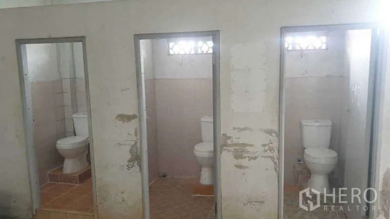 Shophouse for rent in Phra Khanong, Bangkok - Row of three toilet cubicles with white ceramic toilets and unfinished walls.
