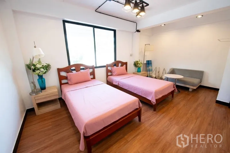 Home Office for rent or sale in Phra Khanong, Bangkok - Spacious twin bedroom with pink bedding, sofa and wood flooring.