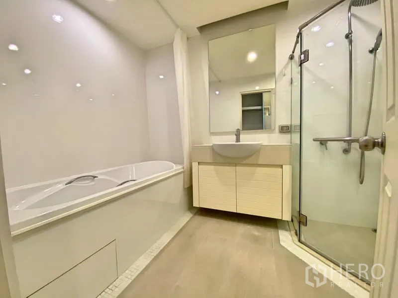 Condominium for rent in Khlong Toei, Bangkok - Bathroom with bathtub, glass shower enclosure, vanity and large mirror.