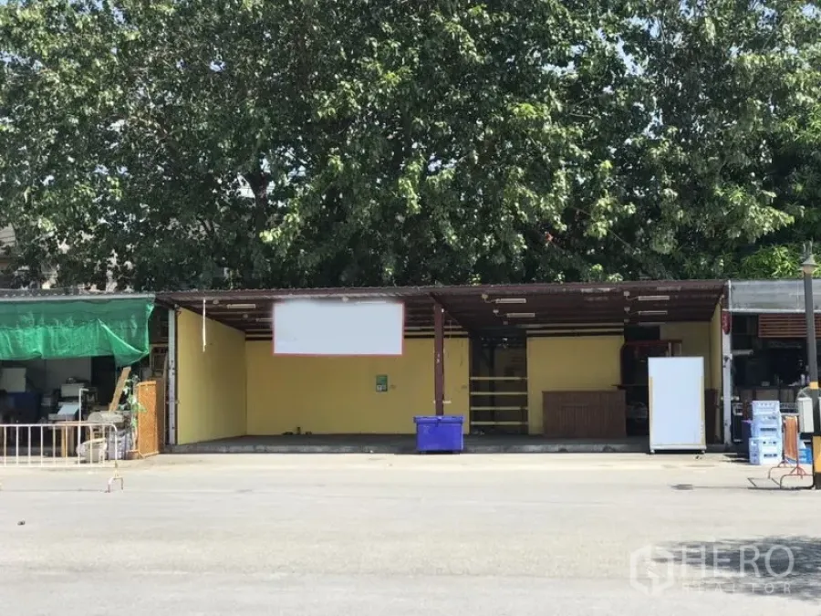 Retail Space for rent in Bang Rak, Bangkok - Open-front retail unit with yellow walls, metal awning, wide street frontage and a paved forecourt shaded by large trees.