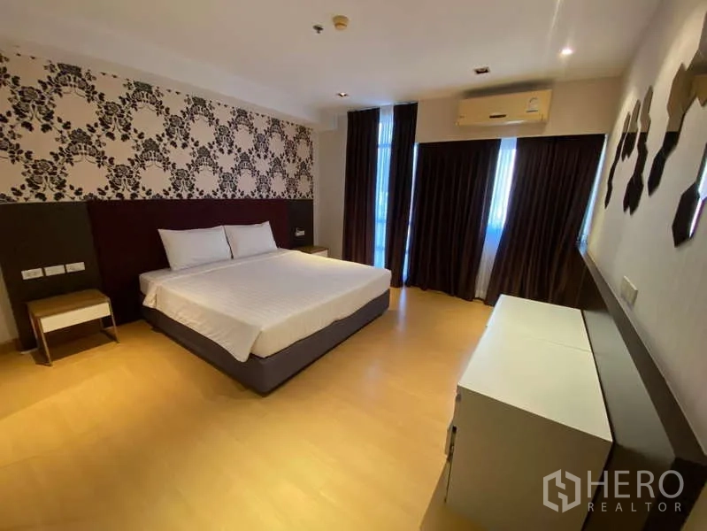 Condominium for rent in Khlong Toei, Bangkok - Master bedroom with king bed, patterned feature wall, blackout curtains, wood floors and air conditioning.