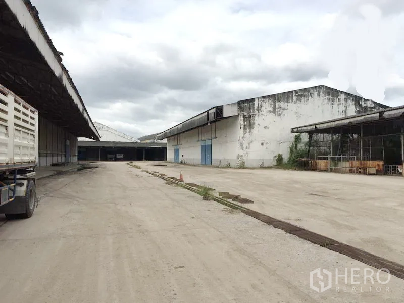 Warehouse for rent in Pathum Thani - External loading area with multiple warehouse buildings, blue doors and wide access for heavy trucks.