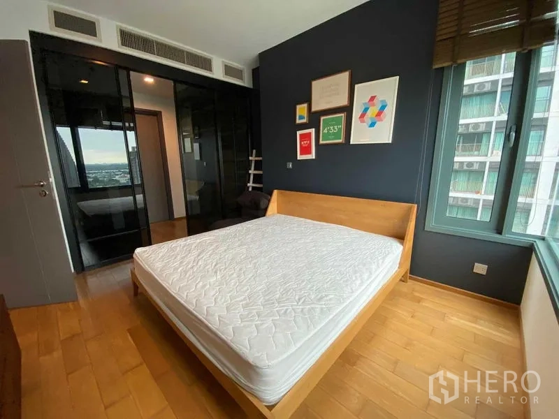 Condominium for rent in Khlong Toei, Bangkok - Bedroom view highlighting glossy built-in wardrobes and natural light from the window.