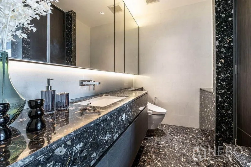 Condominium for rent in Khlong Toei, Bangkok - Modern bathroom with long black marble vanity, backlit mirror and toilet