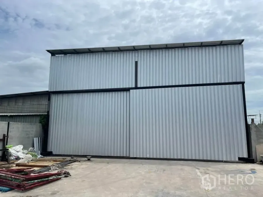 Warehouse for rent or sale in Khlong Luang, Pathum Thani - Front view of a metal-clad warehouse with tall sliding doors and a wide concrete yard.
