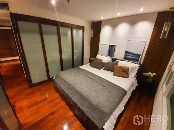 Condominium for rent or sale in Pathum Wan, Bangkok - Primary bedroom with king bed, wood flooring, frosted glass sliding wardrobes and recessed lighting.