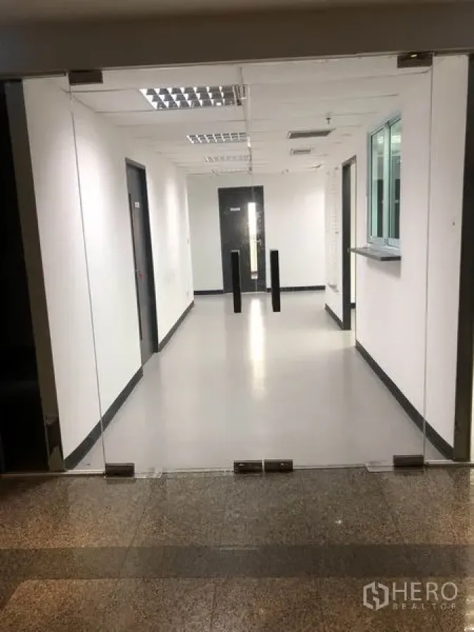 办公空间 出租在Watthana, Bangkok - 玻璃入口通向明亮的办公走廊，白色墙面与通道隔挡。