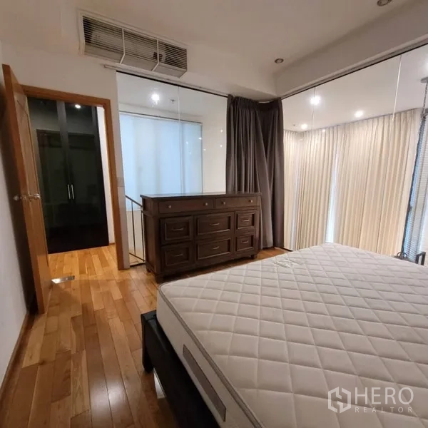 Condominium for rent in Khlong Toei, Bangkok - Bedroom corner with dresser, windows, and warm wood flooring.