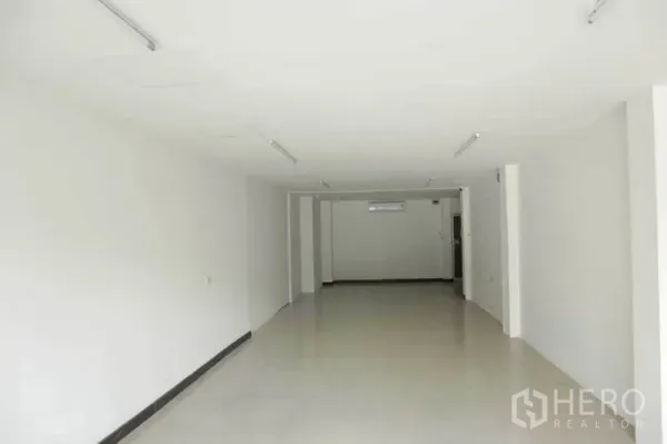 Retail Space for rent in Watthana, Bangkok - Long retail hall with white walls, tiled flooring, ceiling lights, and an air-conditioning unit at the rear.