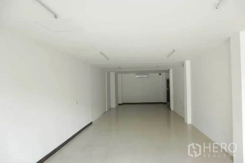 Retail Space for rent in Watthana, Bangkok - Long retail hall with white walls, tiled flooring, ceiling lights, and an air-conditioning unit at the rear.