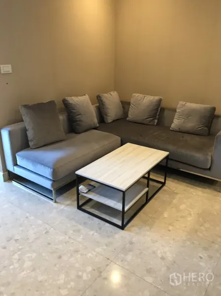 Condominium for rent in Khlong Toei, Bangkok - Cozy living area with L-shaped gray sofa and light wood metal-frame coffee table.