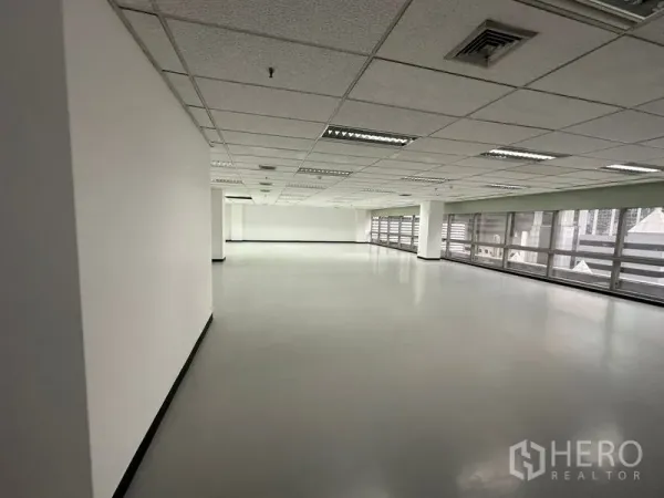 Office Space for rent - Open-plan office floor with drop ceiling lights and long windows along one side.