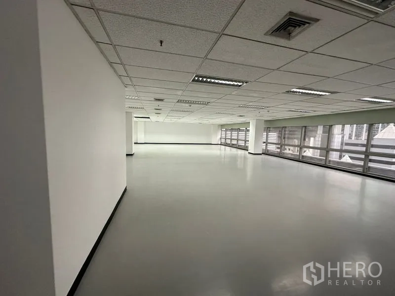 Office Space for rent - Open-plan office floor with drop ceiling lights and long windows along one side.