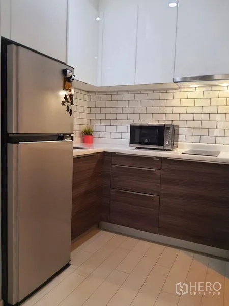 Condominium for rent in Pathum Wan, Bangkok - Compact L-shaped kitchen with white subway tile backsplash, refrigerator and microwave.