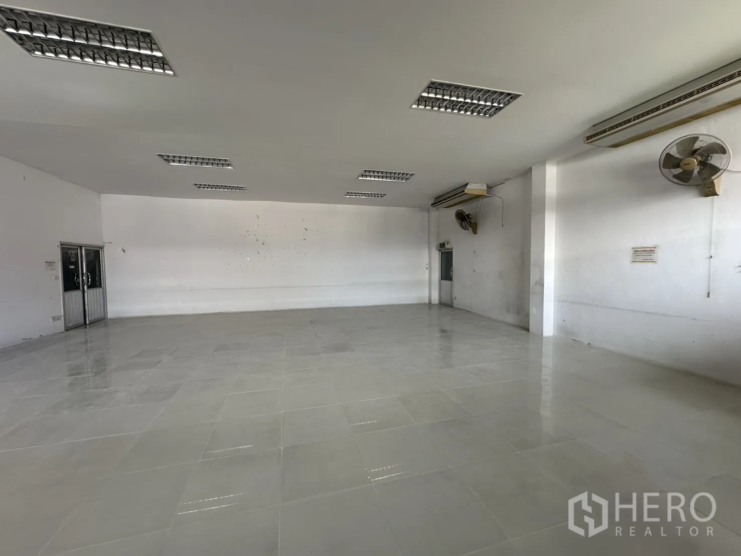 Factory for rent - Large tiled office room with ceiling AC units and fans.