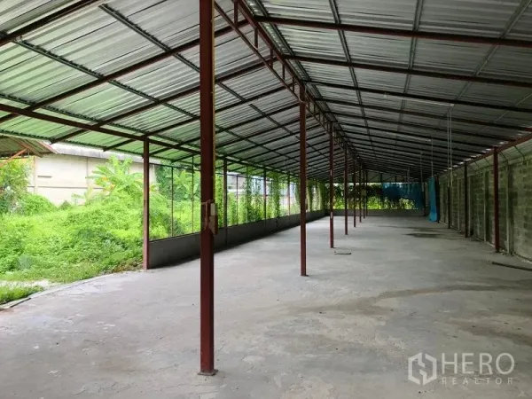 Warehouse for rent in Bang Kapi, Bangkok - Covered loading and work area with metal roof and open sides next to greenery.