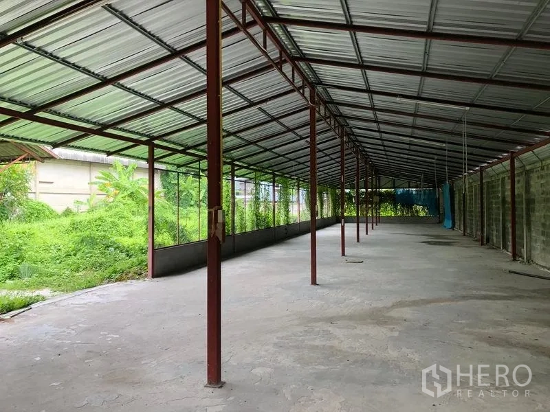 Warehouse for rent in Bang Kapi, Bangkok - Covered loading and work area with metal roof and open sides next to greenery.