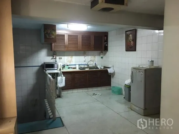 Shophouse for rent in Phra Khanong, Bangkok - Tiled kitchen with wooden cabinets, sink, microwave, and refrigerator.