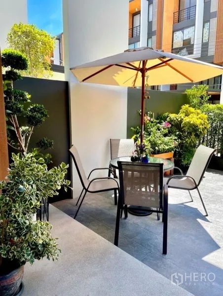 Townhouse for rent in Suan Luang, Bangkok - Cozy front patio with an umbrella table, chairs, and lush greenery.