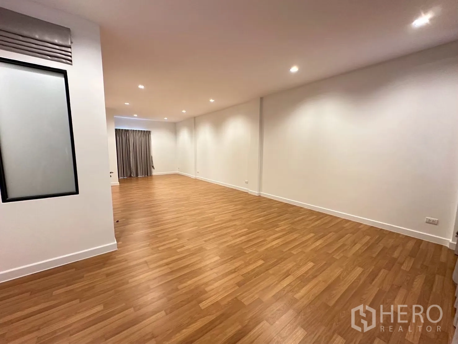 Home Office for rent in Lat Phrao, Bangkok - Spacious upper-floor room with wood flooring, recessed ceiling lights, and curtains.