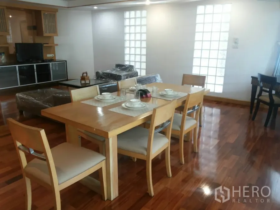 Apartment for rent in Khlong Toei, Bangkok - Open-plan living and dining area with six-seat wooden table, TV cabinet, and polished hardwood floors.