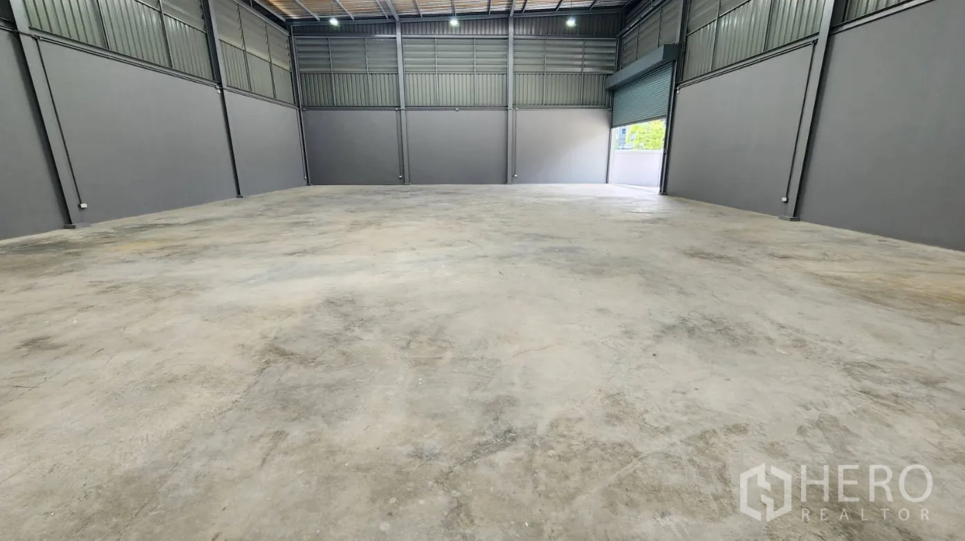 Factory for rent in Bang Bo, Samut Prakan - Spacious warehouse with an open roller door to the loading yard and LED lighting overhead.