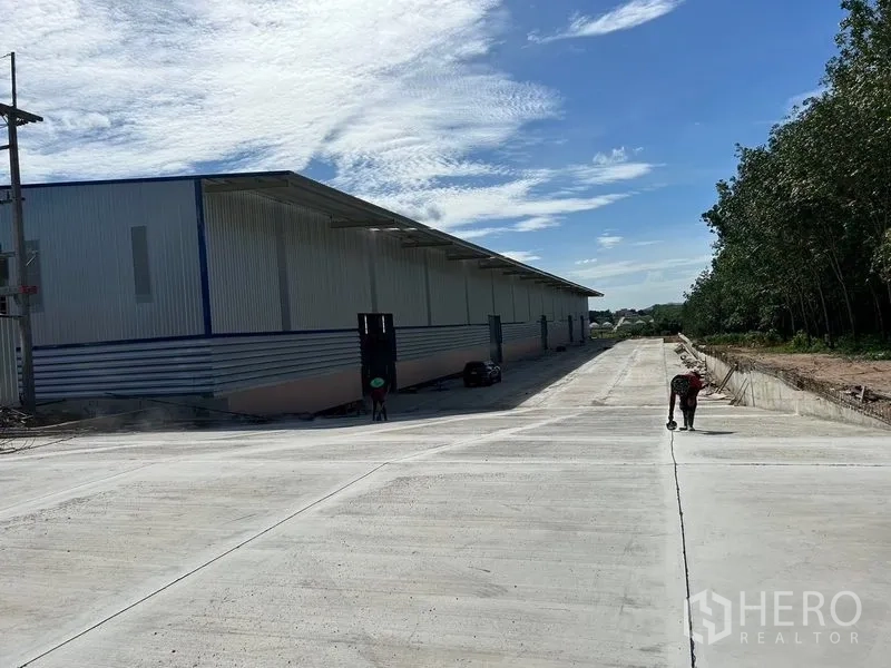 Warehouse for rent in Nikhom Phatthana, Rayong - Long warehouse facade with covered loading bays and a wide concrete driveway designed for truck access.
