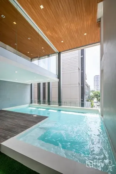 Townhouse for rent in Khlong Toei, Bangkok - Indoor-outdoor plunge pool with high ceiling and wood panels.