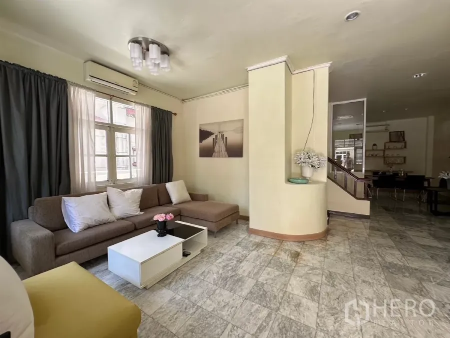 Home Office for rent in Suan Luang, Bangkok - Bright living area with L-shaped sofa, coffee table, and curtained windows.