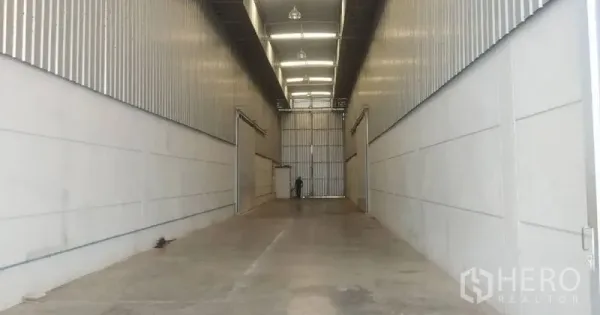 Warehouse for rent in Pathum Thani - Long loading bay corridor with metal cladding and overhead lighting leading to a large door.