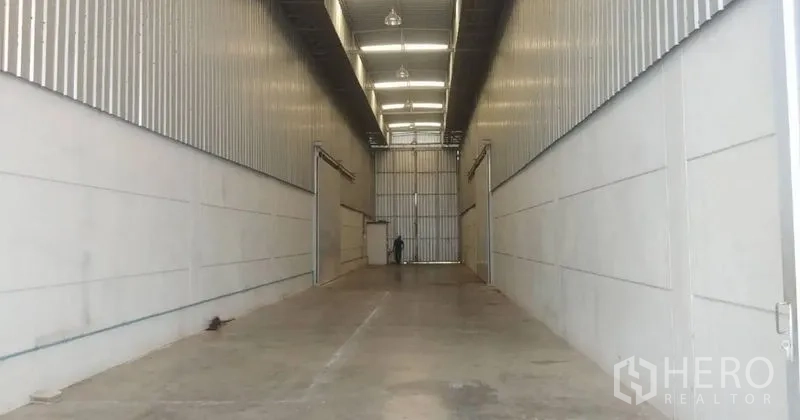 Warehouse for rent in Pathum Thani - Long loading bay corridor with metal cladding and overhead lighting leading to a large door.