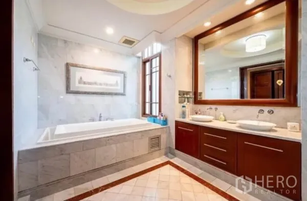 Detached House for rent in Khlong Toei, Bangkok - Elegant marble bathroom with built-in bathtub, double vanity and a large framed mirror.