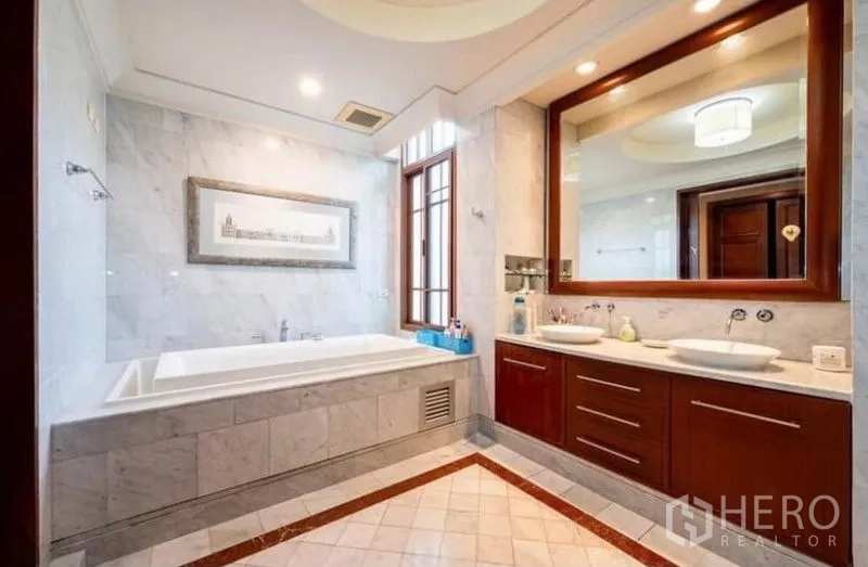 Detached House for rent in Khlong Toei, Bangkok - Elegant marble bathroom with built-in bathtub, double vanity and a large framed mirror.