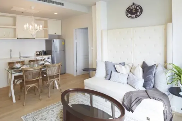 Condominium for rent in Bangkok - Open-plan living and dining area with chandelier and compact kitchen.