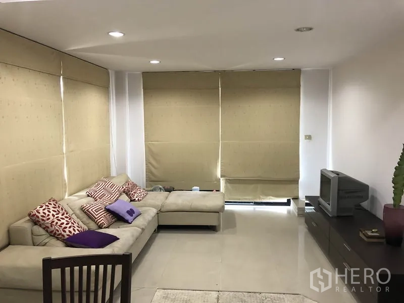 Home Office for rent in Wang Thonglang, Bangkok - Cozy living area with L-shaped sofa, TV console, tiled floor and large roller blinds.