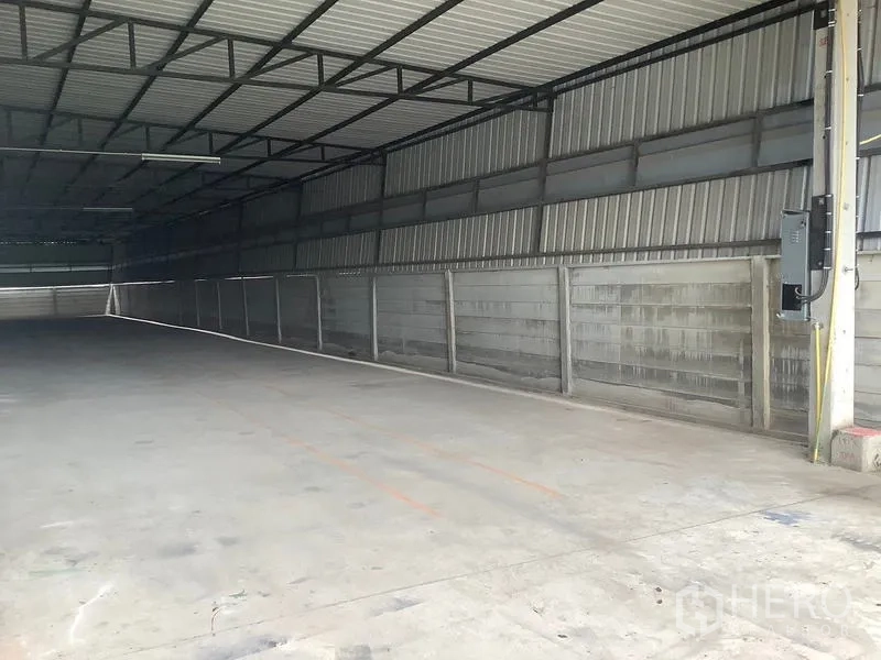 Factory for rent in Ban Phaeo, Samut Sakhon - Concrete loading aisle beneath steel roof and translucent panels.