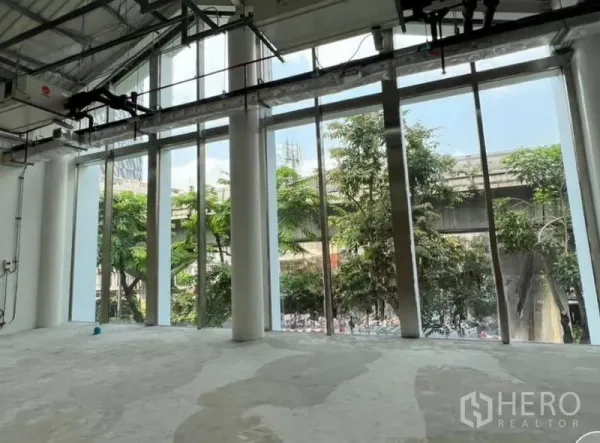 Retail Space for rent in Phaya Thai, Bangkok - Wide glass frontage with double‑height ceiling and views to street trees and an elevated transit line outside.