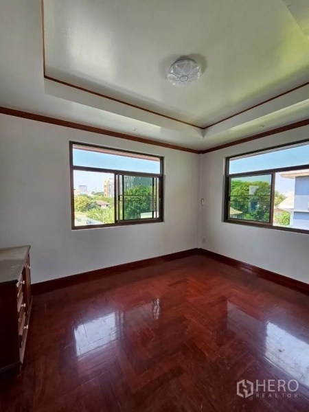 Home Office for rent in Wang Thonglang, Bangkok - Corner bedroom with two large sliding windows and glossy parquet flooring overlooking trees.