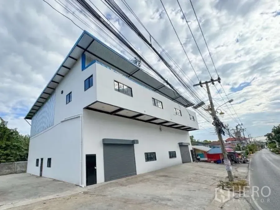 货栈 出租在Bang Phli, Samut Prakan - 现代两层仓库外观，白色立面，双卷闸门，宽阔混凝土前场，临安静道路（邦普里）。