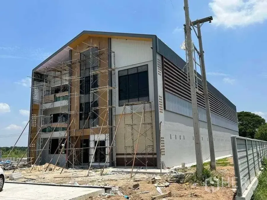 工厂 出售在Khlong Luang, Pathum Thani - 工厂外立面施工中，脚手架围绕，山墙屋顶与卷闸门。