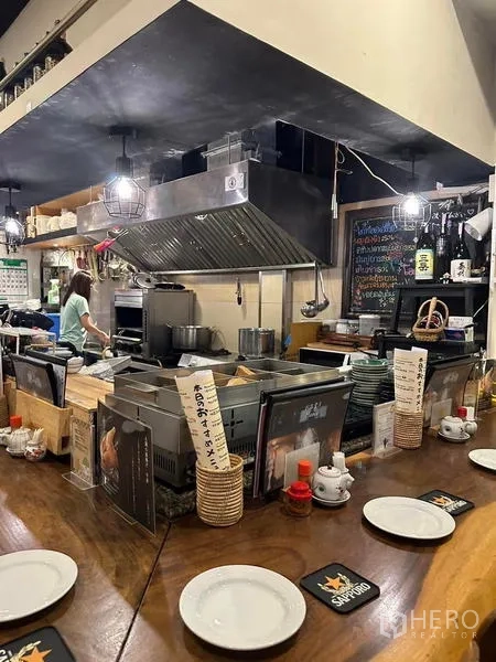 Shophouse for rent or sale in Watthana, Bangkok - Restaurant‑fitted open kitchen with stainless extraction hood, counter equipment and pendant lighting.