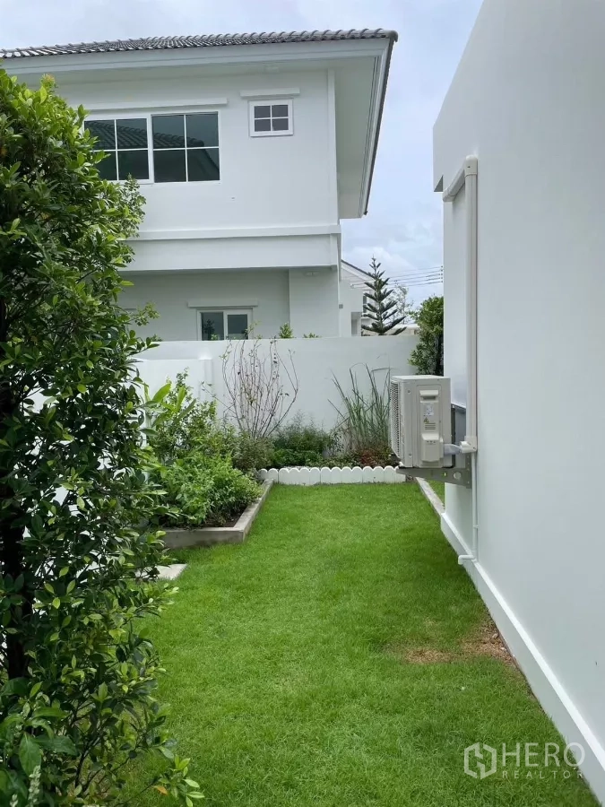 Detached House for rent in Bang Phli, Samut Prakan - Side garden with green lawn, planter beds, and a white boundary wall.