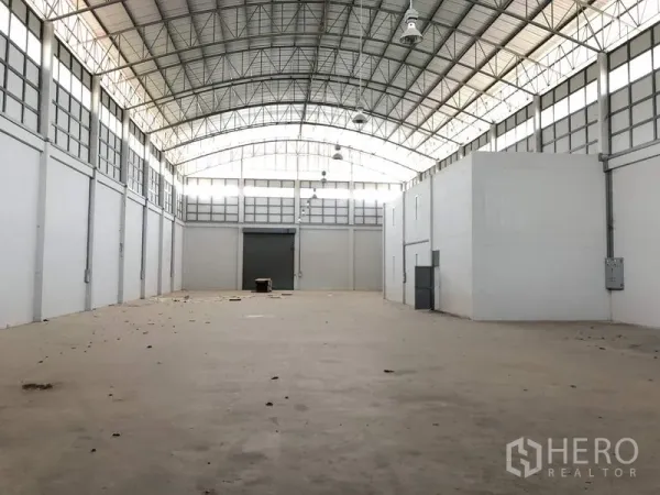 Factory for rent in Lam Luk Ka, Pathum Thani - Spacious warehouse interior with high arched steel roof, skylights, concrete floor and a large roller door.