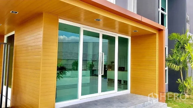 Warehouse for sale in Lam Luk Ka, Pathum Thani - Glass‑front office entry with wood canopy and sliding doors at the front of the building.
