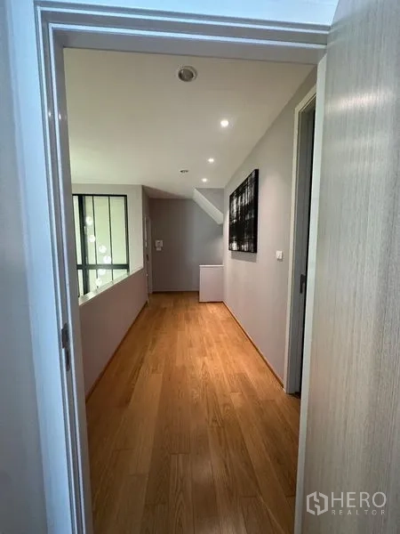 Townhouse for sale in Saphan Sung, Bangkok - Upper-floor corridor with wood flooring, soft grey walls and ceiling spotlights.